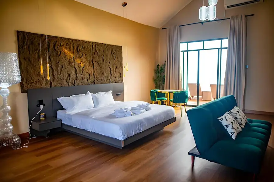 Spacious and modern interior of the Bedroom Deluxe 1 Bed at Turtle Seaweed Resort featuring a comfortable bed, teal sofa, and access to an ocean-view balcony.
